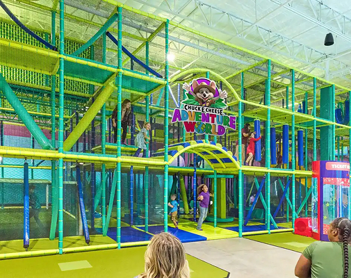 A multi-story indoor play structure of nets, walkways and slides under the Adventure World sign, with kids climbing through it