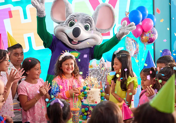 The birthday kid holding their cake as friends and Adventure Chuck E. celebrate around them