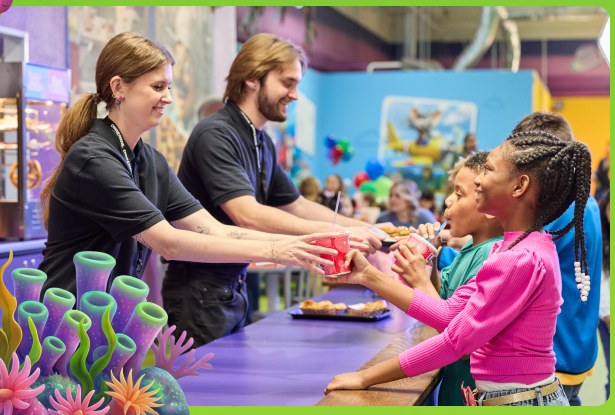 Adventure World team members handing snacks across the counter to two kids