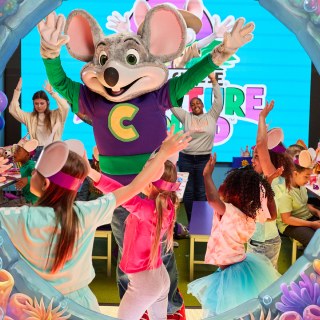 Chuck E. leading a live show for a room of kids in front of the giant video wall