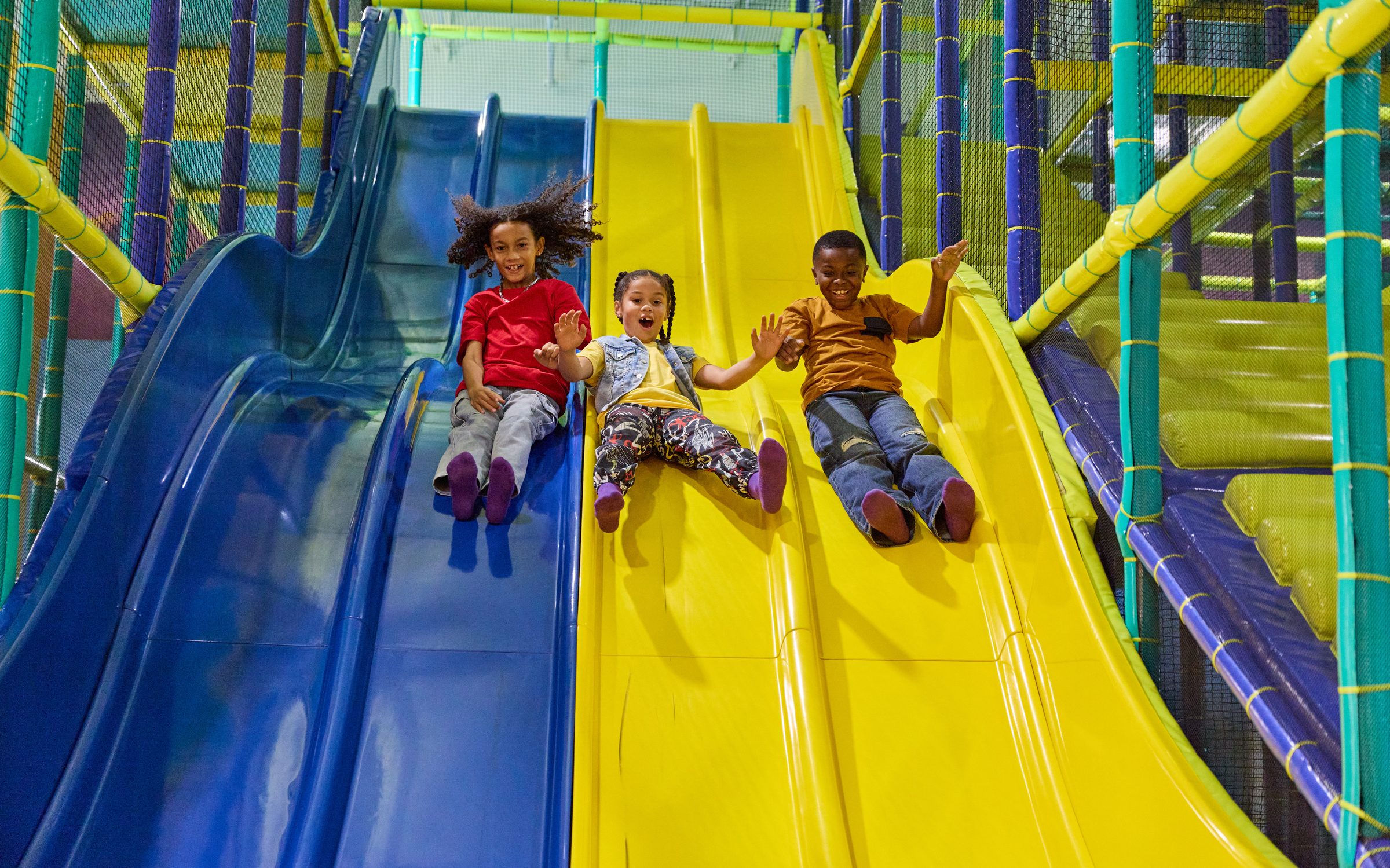 Three kids racing down the twin slides at Chuck E. Cheese Adventure World