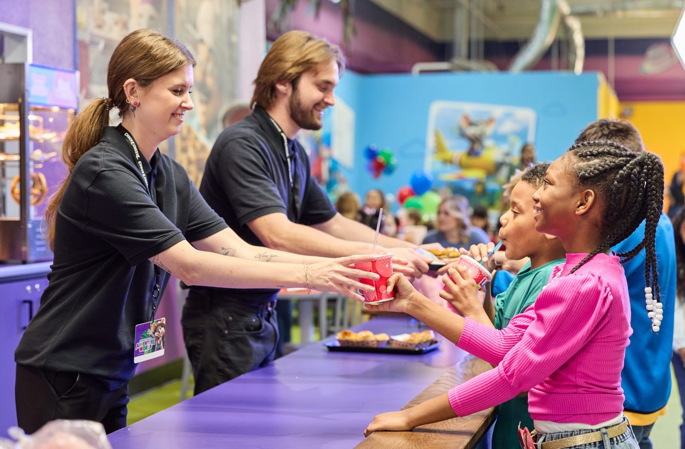 Adventure World team members handing snacks across the counter to two kids
