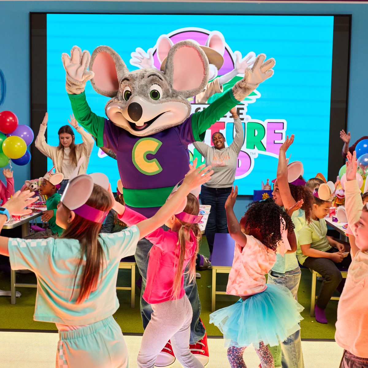 Chuck E. leading a live show for a room of kids in front of the giant video wall
