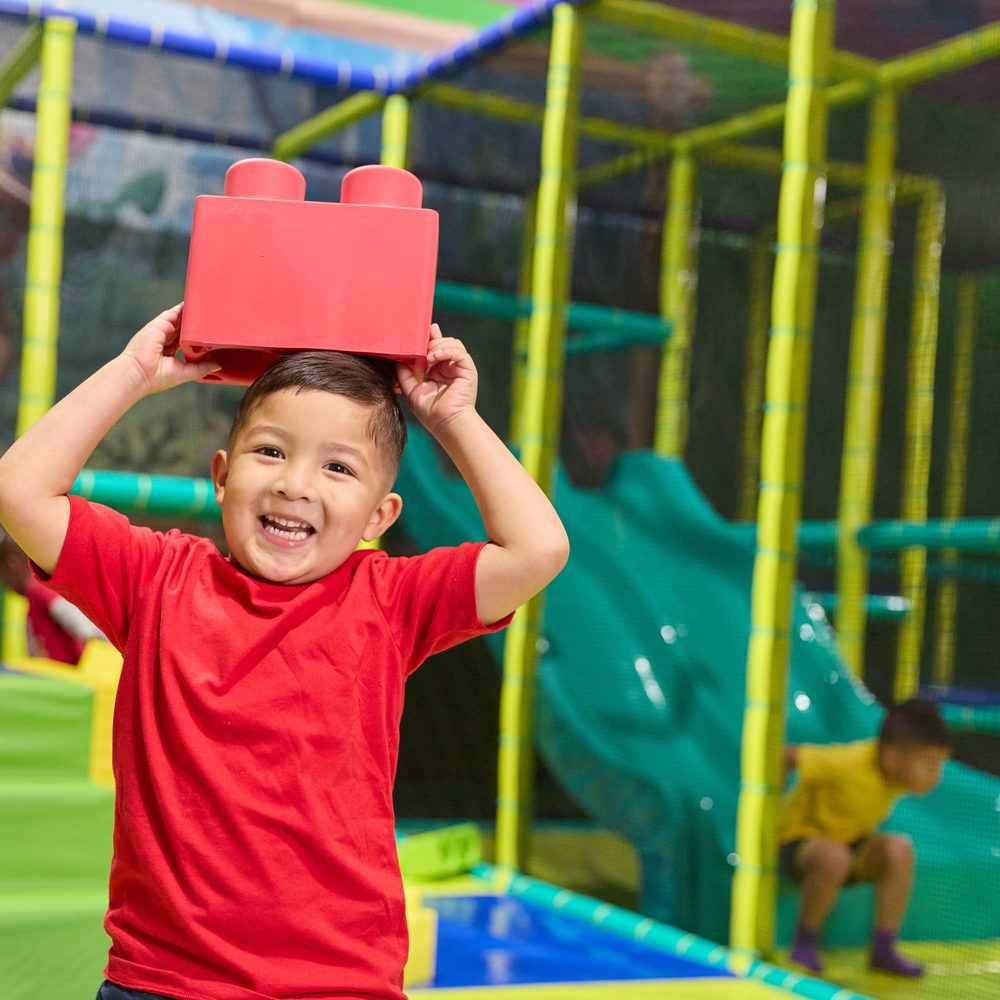 A boy balancing a foam block on his head inside the Adventure World play structure