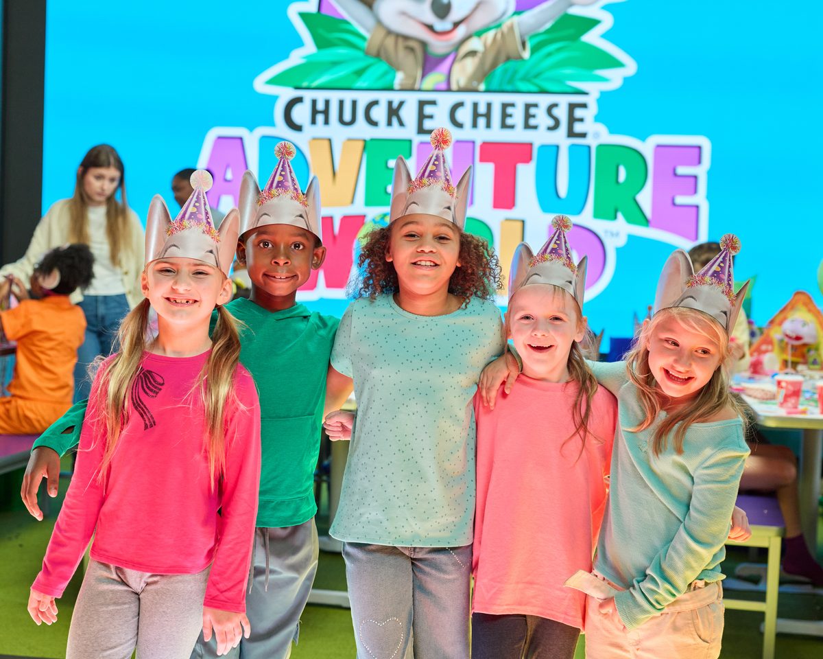 Kids in party hats lined up in front of the Adventure World video wall