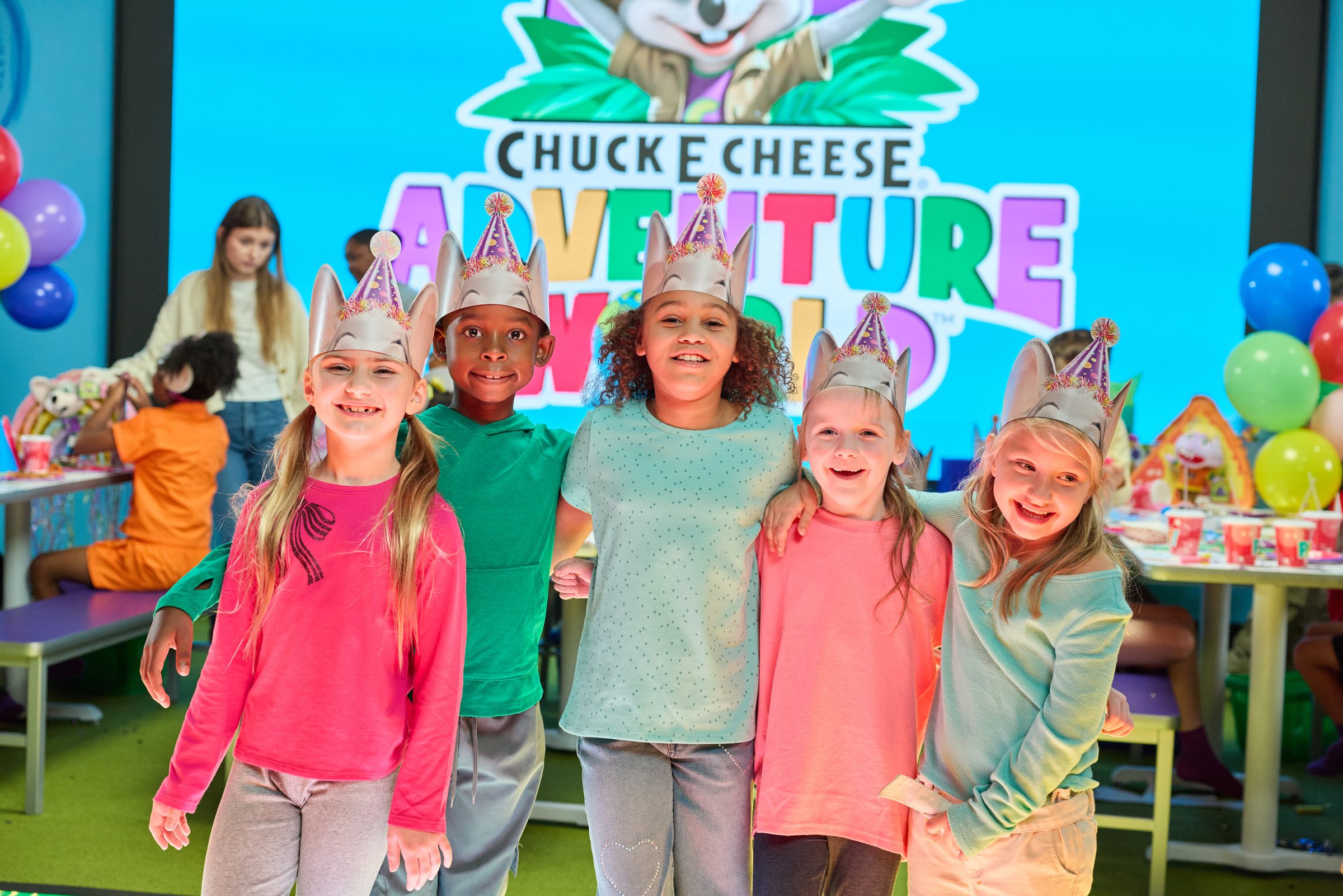 Kids in party hats lined up in front of the Adventure World video wall