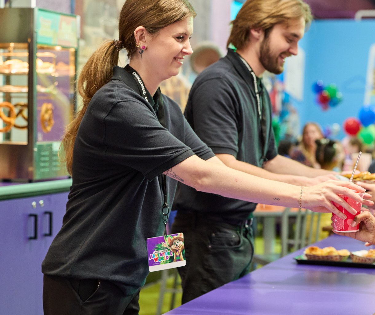 Adventure World team members handing snacks and drinks across the Power Up Station counter to a line of kids