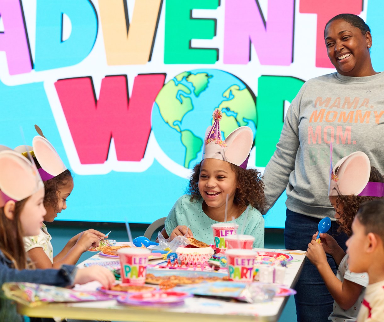 A birthday group around a decorated party table in front of the Adventure World wall